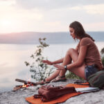 Hipster young girl with backpack enjoying sunset on peak of rock mountain. Tourist traveler on background view mockup